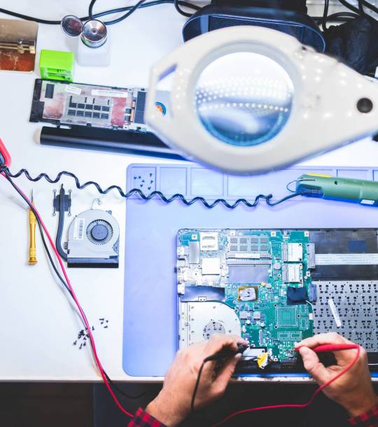 Side view of crop young concentrated guy repairing laptop and sitting at table between different gadgets and tools